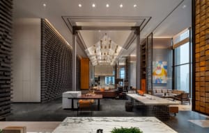 A spacious, modern lobby features a grand marble reception desk, metal chandelier, and contemporary seating.
