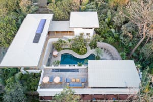 An aerial view of a modern residential house featuring a concrete pool surrounded by a lush tropical garden.