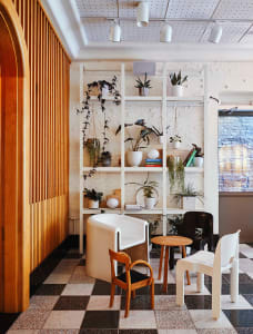Modern restaurant cafe interior with hanging plants, white shelves, and wooden furniture.
