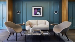 Modern living room with dark blue panel walls, white fabric sofa, two beige armchairs, marble coffee table, and abstract art 