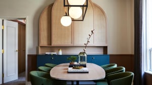 A modern meeting room featuring a round table with green upholstered chairs, a wooden table, and a rattan accent wall.