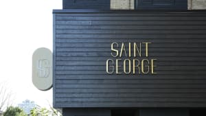The exterior facade of a modern building with a black wooden exterior and a gold sign reading 'SAINT GEORGE'.