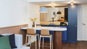 Modern kitchen with blue wood and marble bar, featuring sleek bar stools and white seating area with green and blue accents.