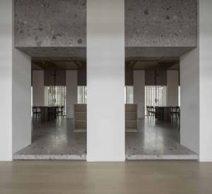 Modern restaurant interior with concrete floors and walls, featuring tables and chairs.