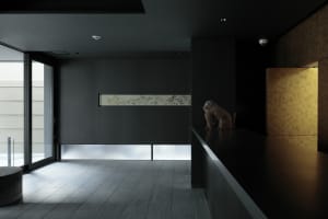 A minimalist interior with concrete walls, a black floor, and a small sculpture.