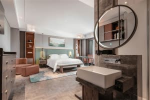 Modern bedroom with minimalist furniture, a large round mirror, a comfortable bed, and a vanity area with a rectangular sink 