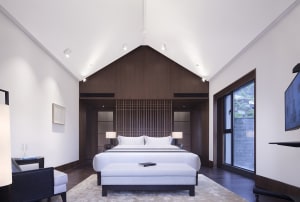 A minimalist bedroom with a large white bed, wooden headboard, and glass panels.