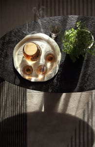 A modern coffee table setting with a glass teapot and cups, placed on a black stone surface.