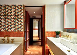 Modern bathroom with white tiled walls, orange tiled floor, and gold faucets.