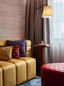 A modern living room featuring a yellow sofa, curtains, and a side table with a plant and books.