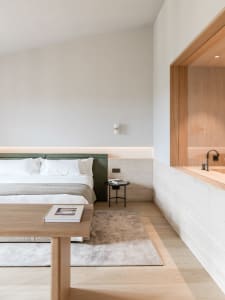 A minimalist modern bedroom featuring a large bed with a green headboard and a wooden table with a book on it.