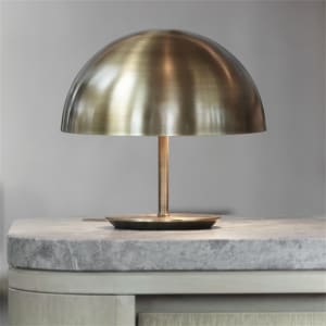 A modern table lamp with a brass dome shade on a marble surface.