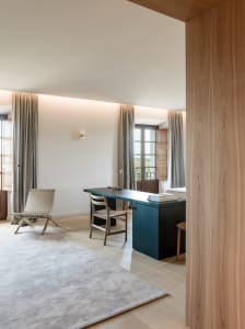 Modern and minimalistic office space featuring a blue desk, wooden chair, and fabric curtains.