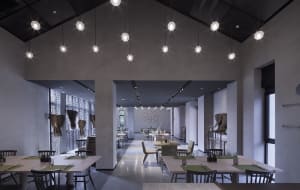 A modern restaurant interior with concrete walls and hanging lights.