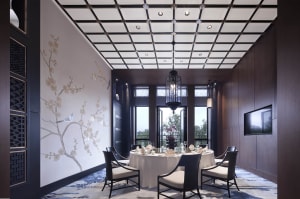 A modern restaurant interior with white walls, black ceiling, and black chairs around a round dining table.