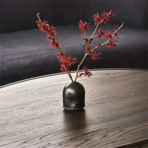 A ceramic vase with red flowers sits on a wooden coffee table in a modern interior setting.