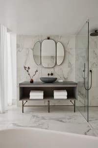 A modern bathroom with marble tile walls and floor, featuring a floating vanity, a black stone sink, and a walk-in shower wit