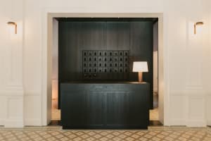 Modern reception desk with dark wooden finish, illuminated by a table lamp and located at the entrance of an elegant lobby.