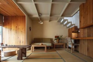 A minimalist living room with wooden furniture, including a sofa, coffee table, and shelf, featuring a natural light source a