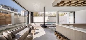 A modern living room featuring a concrete floor and wood accents with a view of a swimming pool through large windows.