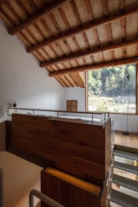 Staircase with wooden railings and floor, featuring a view of greenery through a large window.