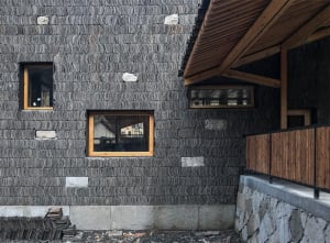 Building facade featuring corrugated metal tiles arranged in a repetitive pattern, with small windows and a wooden overhang.