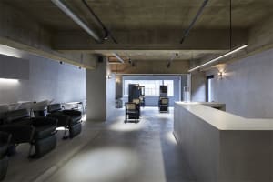 Modern minimalist office space with concrete flooring, exposed concrete walls, and sleek, black chairs.