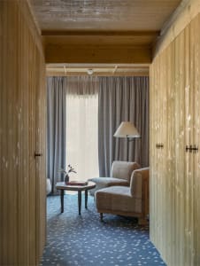 A modern armchair with wooden curtains and a window overlooking a patterned carpet.