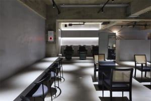 A modern hair salon interior with minimalist design featuring black seating and concrete floors.