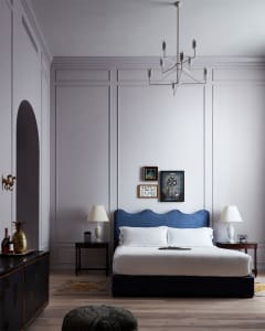 A modern minimalist bedroom with a blue upholstered headboard, wooden flooring, and framed art on the wall.