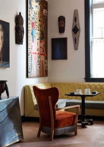 A modern living room featuring an orange upholstered chair with wooden arms and legs, a yellow tufted sofa against the wall, 