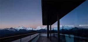 A minimalist balcony with glass walls and a view of snowy mountains.