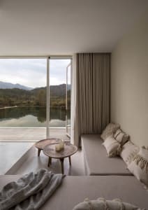 Modern minimalist living room with concrete walls and wooden furniture, featuring a cozy seating area with pillows, a small r