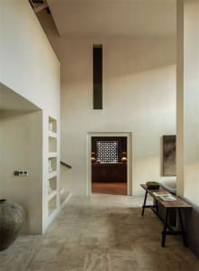 Modern minimalist entrance with concrete and plaster walls, tall ceiling, and wooden bench.