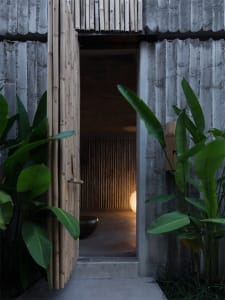An open bamboo doorway constructed with concrete, illuminated by a nearby light.
