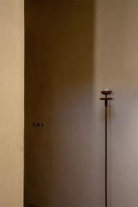 A minimalist entryway featuring a tall, slender metal candlestick with a single white candle.