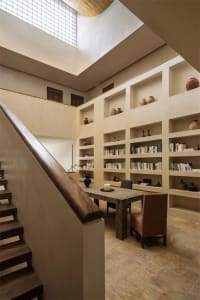 A modern library with concrete shelving and a wooden table surrounded by chairs.