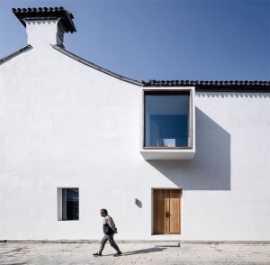A minimalist modern white house with a large glass window and a wooden door on a clear day.