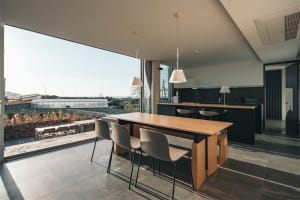 Modern kitchen with concrete and wood materials, featuring a dining table and bar area.