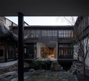 A traditional Chinese garden with wooden beams, glass seating, and stone path.