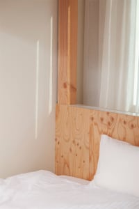 White bed with wooden paneling in a minimalist bedroom setting.