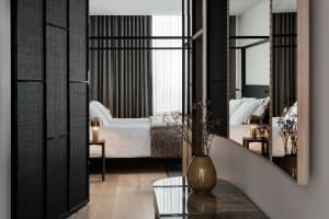 A minimalist bedroom featuring fabric bedding, a wooden floor, and metallic accents.