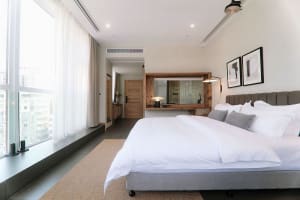 A minimalist bedroom featuring a large white bed, grey headboard, and white walls.