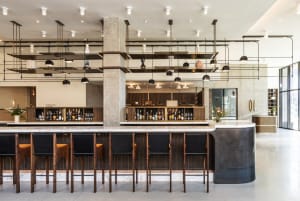 Modern industrial bar with marble countertops, metal stools, and a concrete pillar.