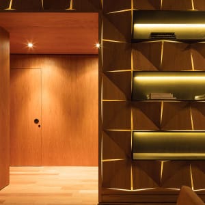 A modern library with a wooden shelf featuring geometric design and built-in lighting.