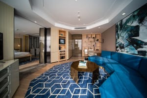 Modern living room featuring a blue sectional sofa, wooden coffee table, and glass panel divider with stainless steel accents