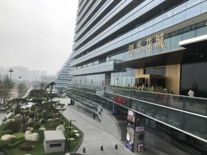 A modern urban building with glass and concrete facade, featuring a landscaped exterior walkway.