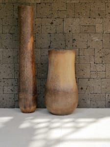 Two wooden vases placed against a textured stone wall.
