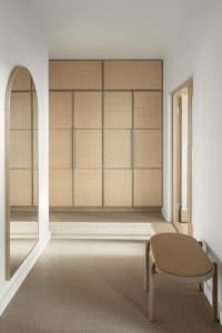 A minimalist bedroom featuring a wooden wardrobe and a cushioned bench.