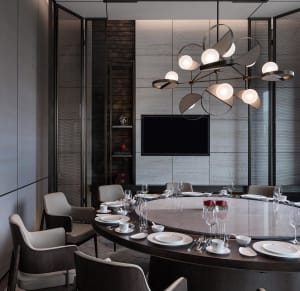 A modern dining room featuring a round table with dishes and glasses, surrounded by white leather chairs, a wooden counter wi